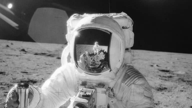  One of the astronauts on the Moon’s surface is holding a container of lunar soil. The other astronaut is seen reflected in his helmet. Apollo 12 safely returned to Earth on November 24, 1969. 