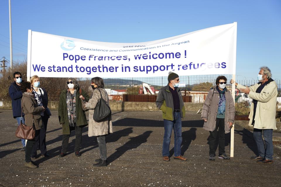 NGO members hold a banner outside Karatepe refugee camp before the visit of Pope Francis, on the northeastern Aegean island of Lesbos, Greece, Sunday, Dec. 5, 2021. Pope Francis is returning to Lesbos, the Greek island that was at the heart of a massive wave of migration into Europe six years ago, after making pointed criticism of European governments on the handling of the crisis during a visit to two hard-hit countries. (AP Photo/Panagiotis Balaskas)