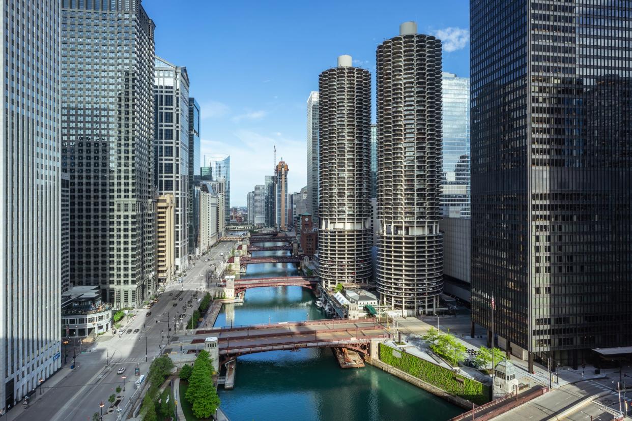 This high angle view looks west down the main branch of the Chicago River. Traffic is seen on Wacker Drive along the river. Featured prominently here are the two identical residential towers of Marina City, which opened in 1963.