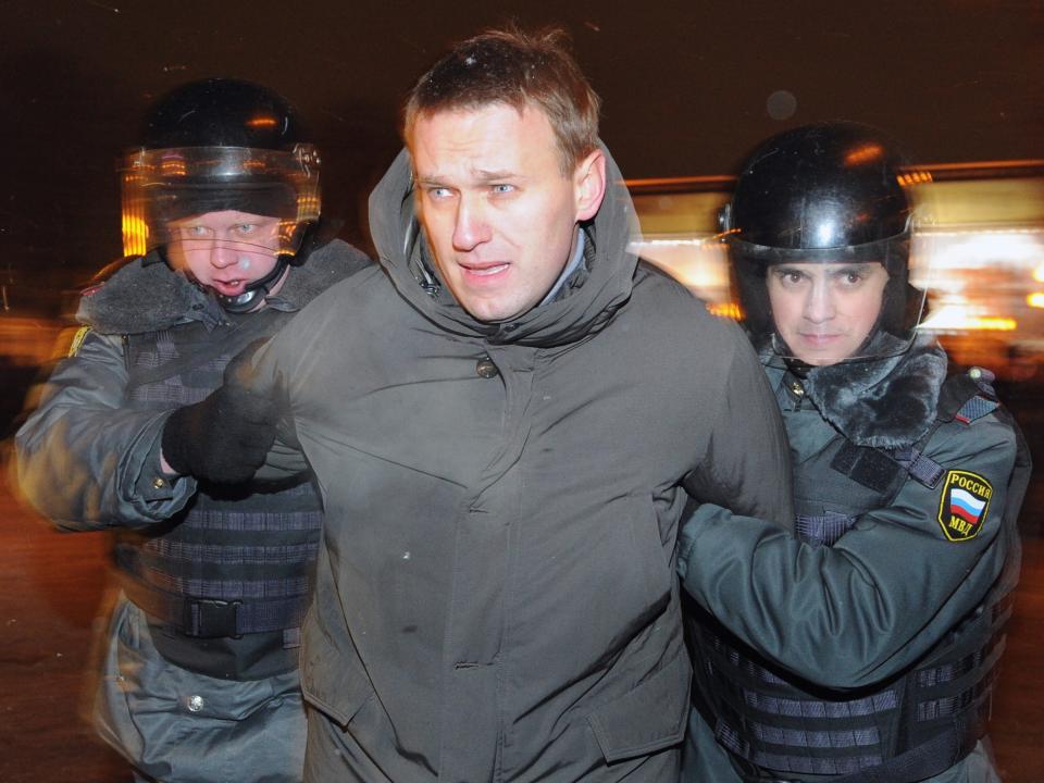 Alexei Navalny with his arms being held behind his back by Russian police officers as he is detained.