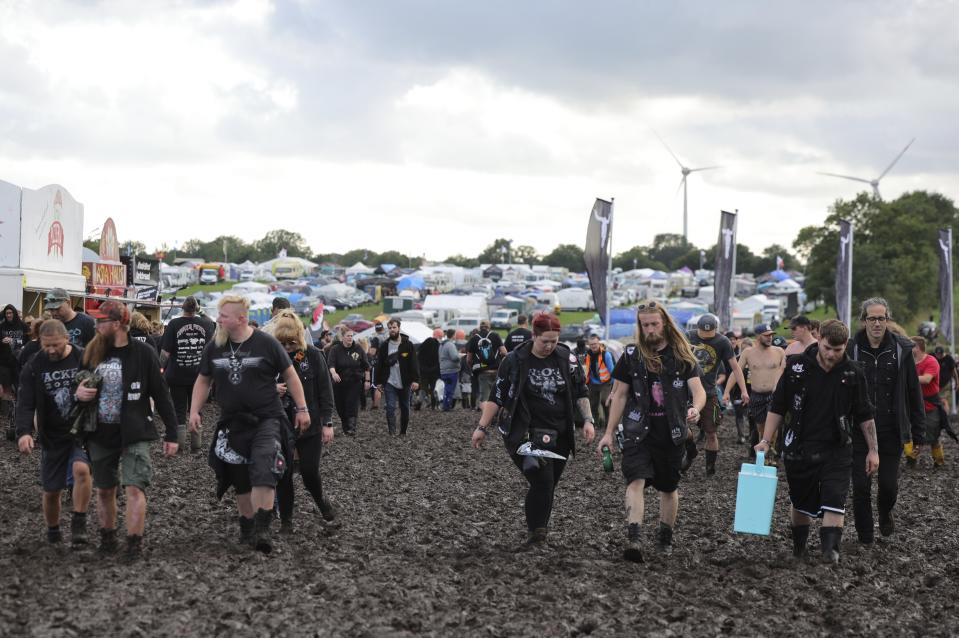 Metal fans walk on the muddy festival grounds ahead of the beginning of the Wacken Open-Air (WOA) Festival, in Wacken, Germany, Tuesday Aug. 1, 2023. WOA Festival takes place from August 2 to August 5, and is considered the largest heavy metal festival in the world. (Christian Charisius/dpa via AP)