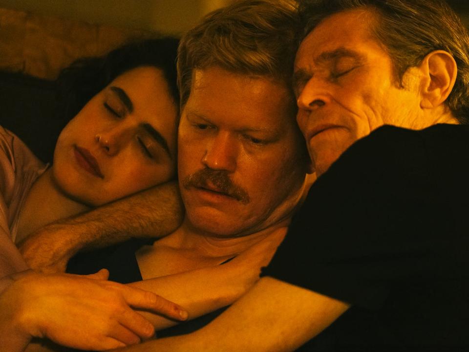 margaret qualley, jesse plemons, and willem dafoe tenderly cuddling together, bathed in warm light, in kinds of kindness. qualley and dafoe look serene, while plemons looks consternation