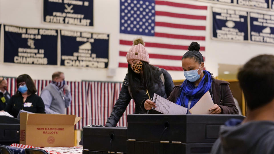 FILE - In this Nov. 3, 2020, file photo, two women, wearing protective masks due to the COVID-19 virus outbreak, cast their ballots at a polling station at Windham, N.H. High School. Regardless of the presidential election outcome, a vexing issue remains to be decided: Will the U.S. be able to tame a perilous pandemic that is surging as holidays, winter and other challenges approach? Public health experts fear the answer is no, at least in the short term, with potentially dire consequences. (AP Photo/Charles Krupa, File)
