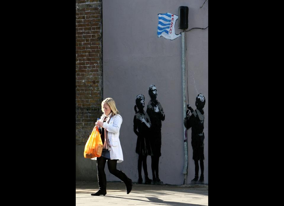 LONDON - MARCH 04:  A lady with a shopping bag passes a recent Banksy work on a wall on March 5, 2008 in London, England. The grafitti shows a child raising a Tesco's plastic bag as a flag. Gordon Brown has said he will force retailers to help reduce the use of plastic bags if they do not take action voluntarily.  (Photo by Cate Gillon/Getty Images)