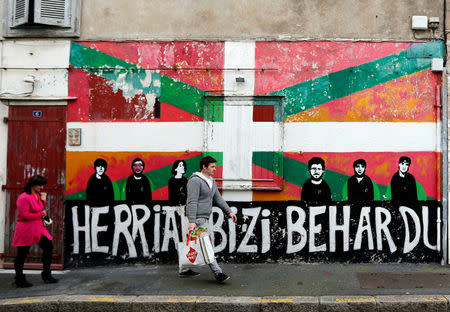 People walk in front of a wall graffiti with a Basque flag painted on of a house in the center of Bayonne, southwestern France, April 7, 2017. Words reads: "The People want to live". REUTERS/Regis Duvignau