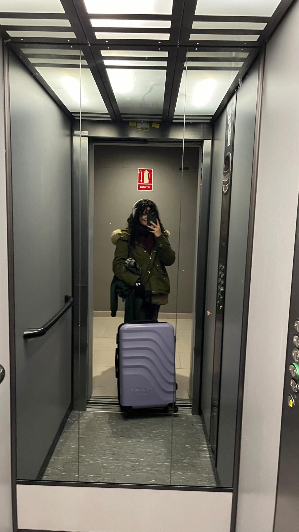 Girl in an elevator standing with purple suitcase