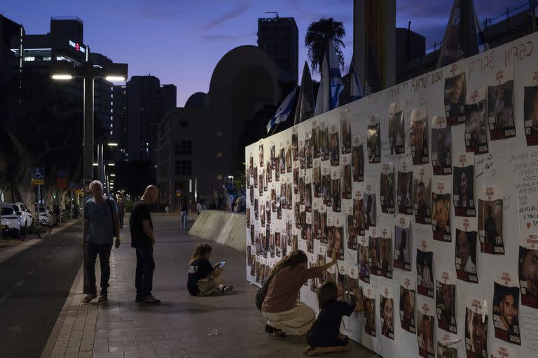 Una mujer israelí toca con la mano fotografías de israelíes desaparecidos y cautivos en Gaza, exhibidas en una pared en Tel Aviv, el sábado 21 de octubre de 2023.