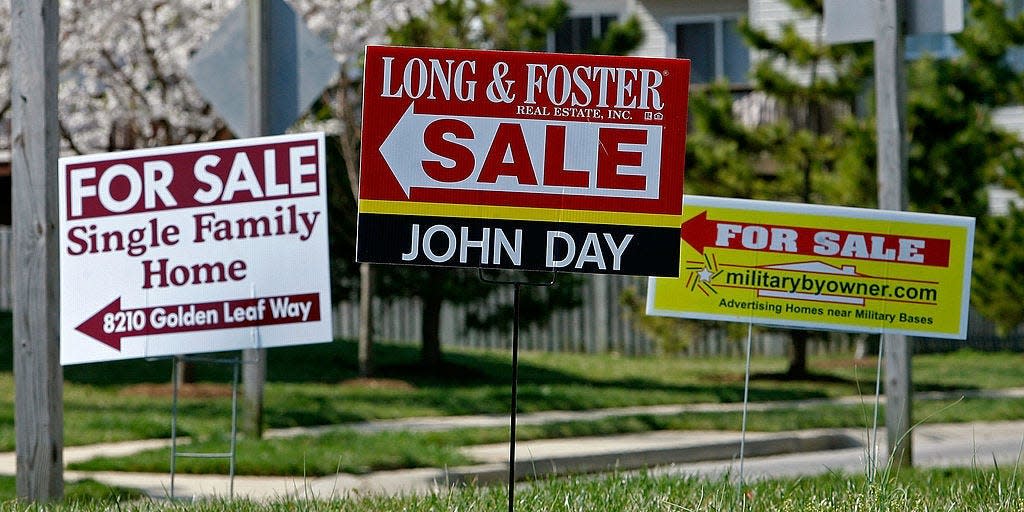 For sale signs stand on a medium strip in a housing development