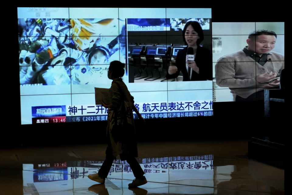 A woman walks by a TV screen showing CCTV broadcasting a news of Chinese astronauts sit inside the Shenzhou-12 manned spacecraft preparing to return to earth, at a shopping mall in Beijing, Thursday, Sept. 16, 2021. (AP Photo/Andy Wong)