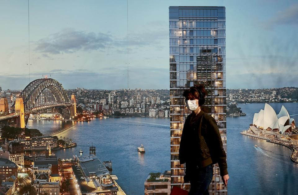 A masked woman walking past a poster of Sydney harbour during the city's ongoing lockdown. Source: Getty