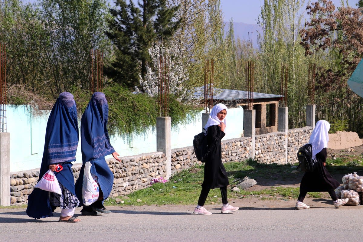 Afghan burqa-clad women along with school girls walk along a road in Fayzabad district of Badakhshan province (AFP via Getty Images)