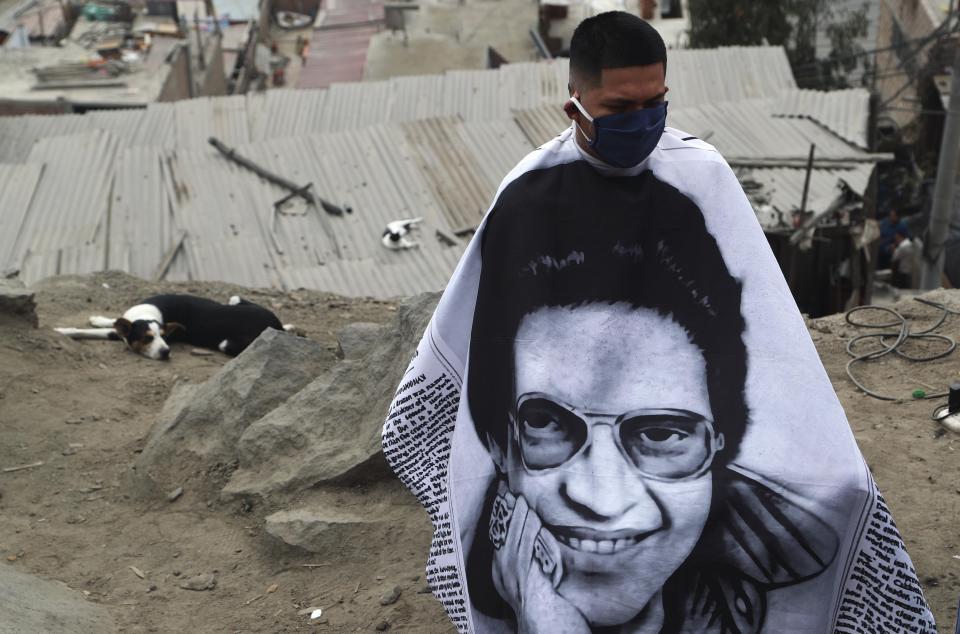 A resident, wearing a barber's apron emblazoned with an image of salsa singer Hector Lavoe, waits to receive a free haircut from Josue Yacahuanca, in the San Juan de Lurigancho poor district of Lima, Peru, Friday, June 19, 2020. Yacahuanca seeks out clients devastated by a quarantine that's gone on for nearly 100 days in an attempt to stem the wave of new coronavirus infections. (AP Photo/Martin Mejia)