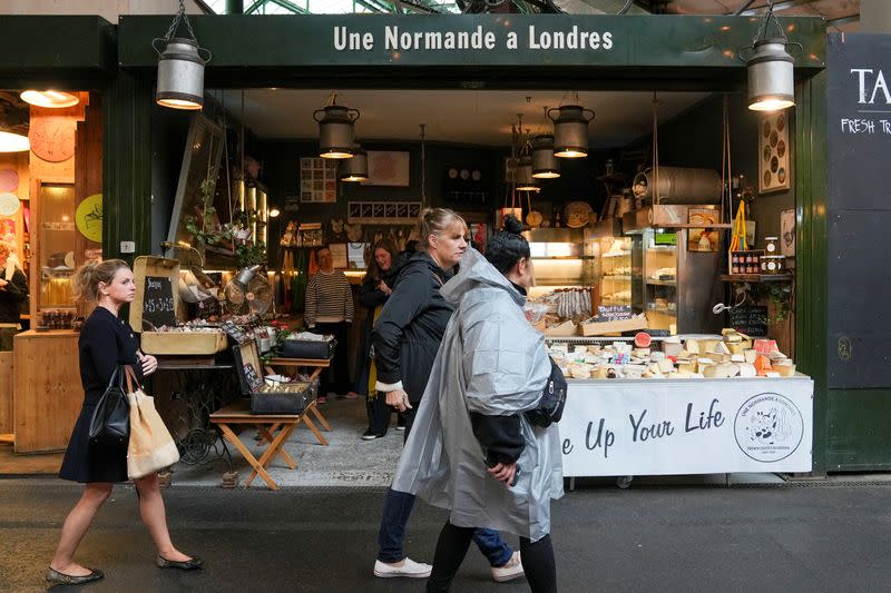 People walk past food stands and market stalls in a Borough Market in London