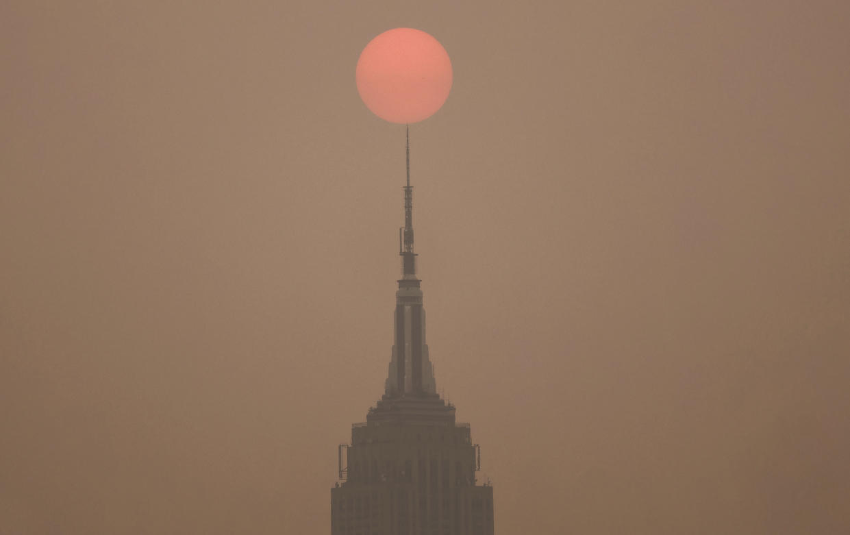 The sun rises in a hazy sky behind the Empire State Building in New York City.