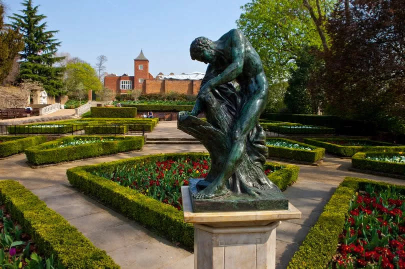 A statue set in formal gardens with flowers in neatly arranged beds