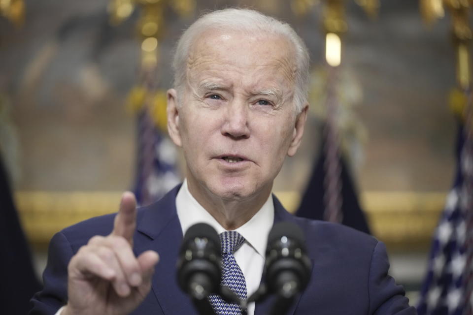 President Biden squints slightly and raises a finger at a podium with two microphones.