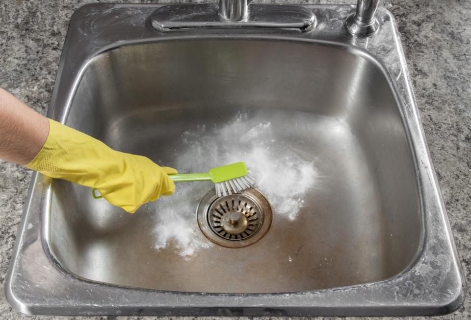 Person with brush scrubbing kitchen sink with powdered cleaner