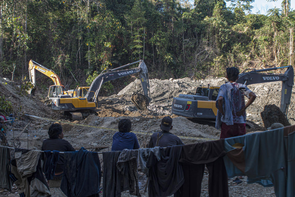 People watch as rescuers use have machines to search for victims at a collapsed gold mine in Parigi Moutong, Central Sulawesi, Indonesia, Thursday, Feb. 25, 2021. The illegal gold mine in Central Indonesia collapsed on miners working inside, leaving a number of people killed, officials said Thursday. (AP Photo/M. Taufan)