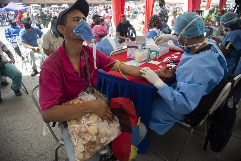 A health worker takes a blood sample for a quick COVID-19 test from man who works selling cookies at the Coche food market in Caracas, Venezuela, Tuesday, June 23, 2020. Health authorities tested people arriving at the market as a preventive measure to help curb the spread of the new coronavirus. (AP Photo/Ariana Cubillos)
