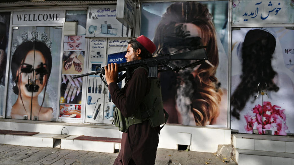 A Taliban fighter walks past a beauty saloon with images of women defaced using a spray paint in Shar-e-Naw in Kabul on August 18, 2021. (Wakil Kohsar/AFP via Getty Images)
