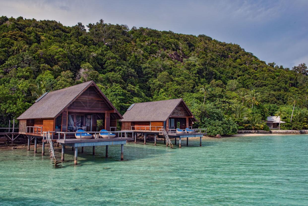 a couple of houses on a dock over water with trees in the background