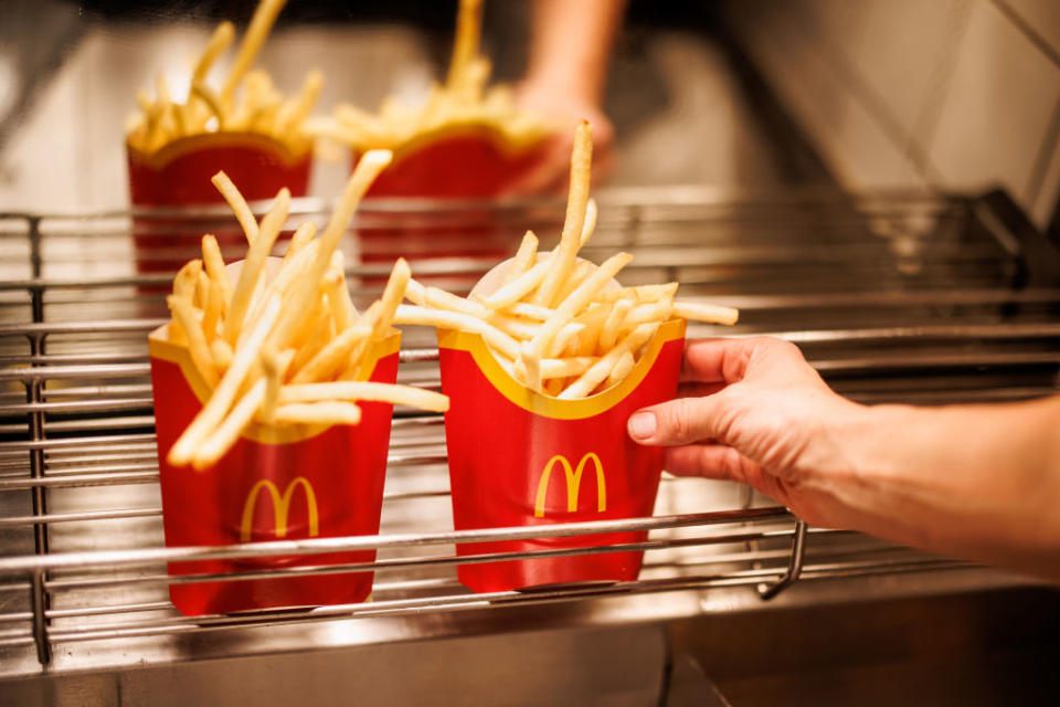 Person holding two containers of McDonald's fries over a metal tray
