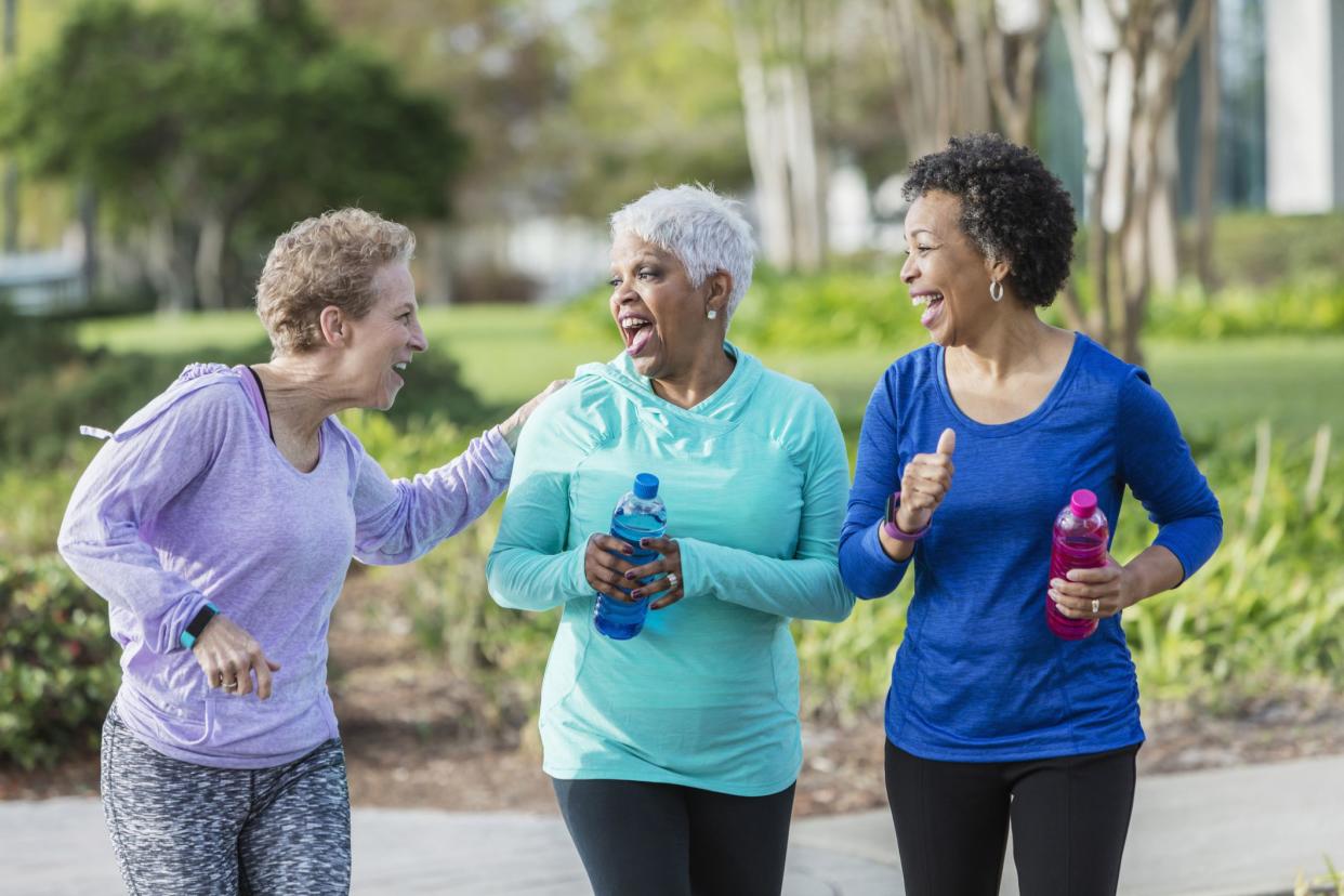 three middle-aged women walking and laughing, carrying water bottles