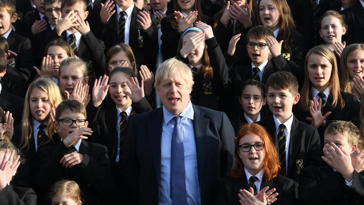 Großbritanniens Premierminister Boris Johnson (M) steht zwischen Schüler bei seinem Besuch eines Colleges.