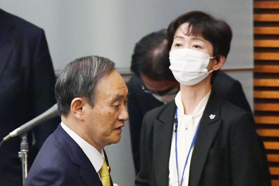 Japanese Prime Minister Yoshihide Suga arrives for a press conference past his cabinet's public affairs official Makiko Yamada, right, at his official residence in Tokyo on Dec. 4, 2020, Yamada, public relations chief for Suga, has resigned Monday, March 1, 2021 after she acknowledged she had a 70,000 yen ($700) dinner paid for by a broadcaster. The broadcaster in question employs Suga’s son, Seigo Suga. (Kyodo News via AP)