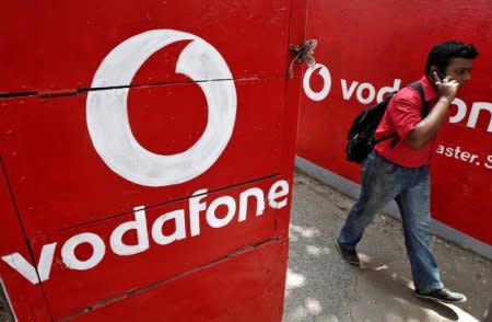 FILE PHOTO: A man speaks on his mobile phone as he walks past logos of Vodafone painted on a roadside wall in Kolkata, May 20, 2014 REUTERS/Rupak De Chowdhuri/File Photo