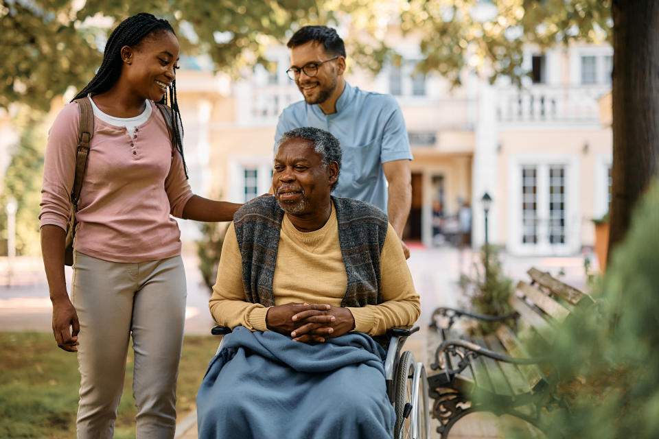 Happy African American senior man in wheelchair talking to his daughter who is visiting him in nursing home.