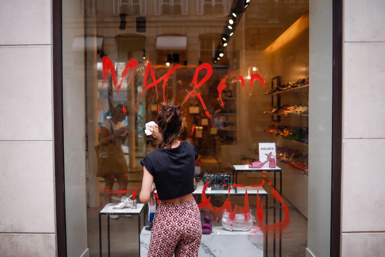 A shopkeeper cleans a Macron graffiti written on the storefront in Paris, France, 30 June 2023 (EPA)