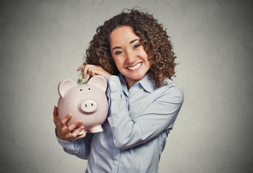 Smiling woman putting money in piggy bank.