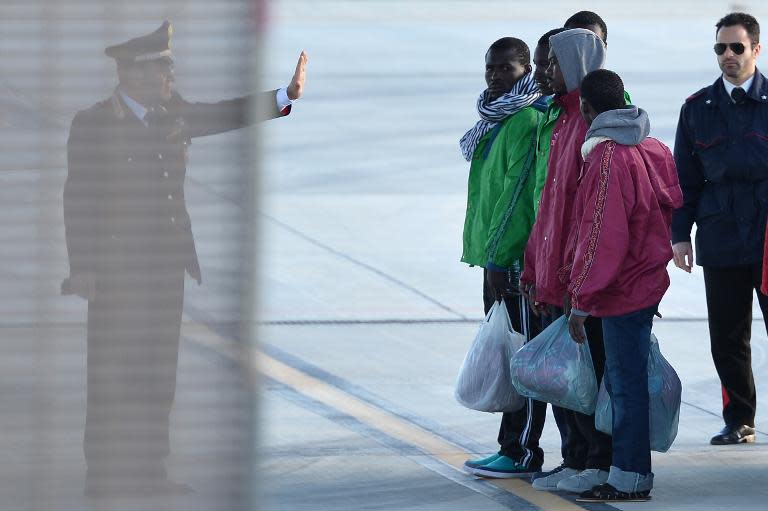 A police officer gives instructions to migrants before they board a military plane to be transferred on February 17, 2015 at the Lampedusa airport