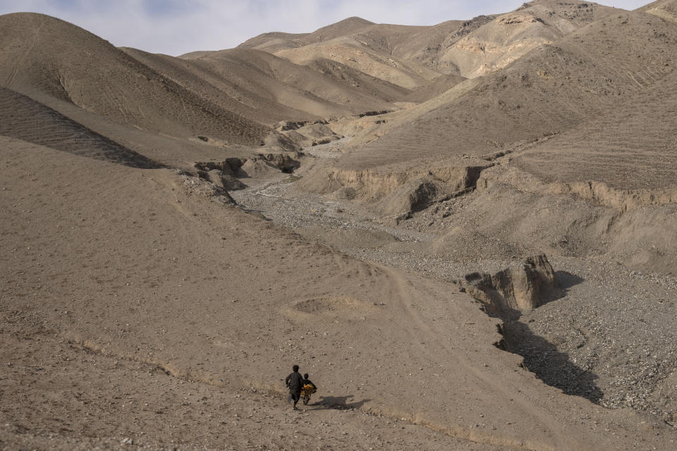 A boy pushes a wheelbarrow with canisters and his younger brother, on their way to collect water from a stagnant pool, about 3 kilometers (2 miles) from their home in Kamar Kalagh village outside Herat, Afghanistan, Friday, Nov. 26, 2021. Afghanistan’s drought, its worst in decades, is now entering its second year, exacerbated by climate change. (AP Photo/Petros Giannakouris)