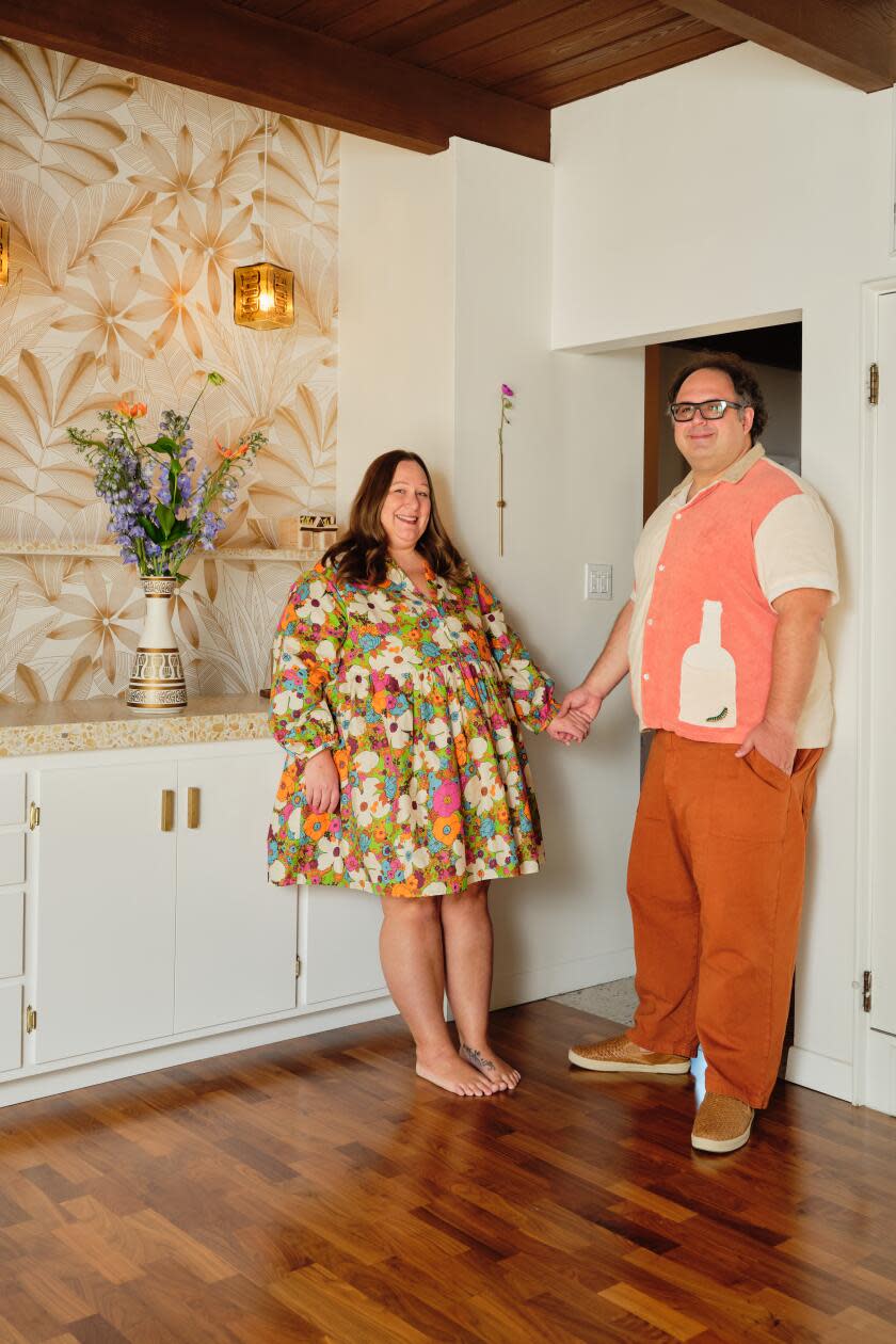 Jessica and Art Martinez hold hands and smile for the camera in front of their tiki bar.