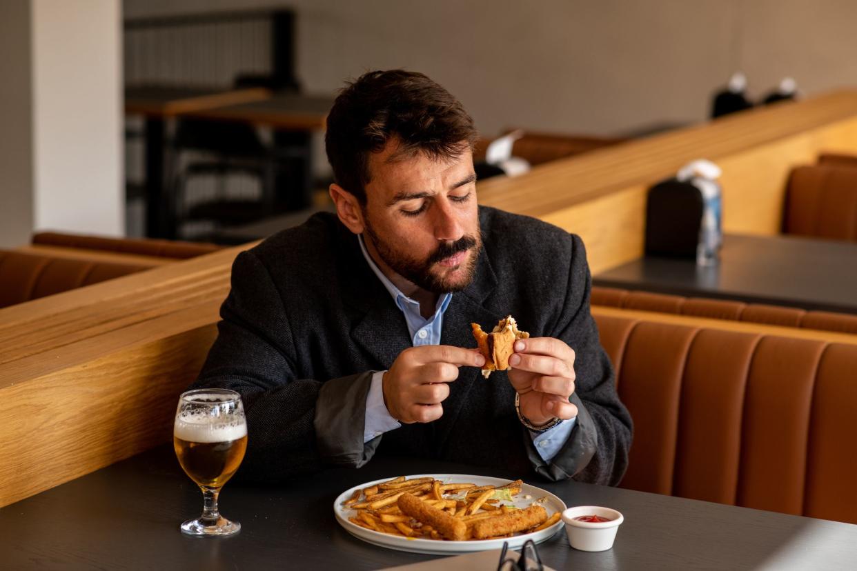 Attractive young businessman eating in a restaurant, while working on his laptop. Young entrepreneur on a business trip, working from his hotel restaurant. Handsome young businessman using modern technology for work.