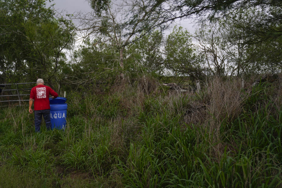 Migrant rights activist Eduardo Canales checks one of his blue water drops Saturday, May 15, 2021, in Falfurrias, Texas. Every week, Canales fills up blue water drums that are spread throughout a vast valley of Texas ranchlands and brush. They are there for migrants who venture into the rough terrain to avoid being caught and sent back to Mexico. (AP Photo/Gregory Bull)