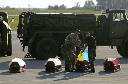 Ukrainian soldiers cover coffins containing the bodies of Ukrainian servicemen killed in action in eastern Ukraine with national flags upon their arrival at the airport in Lviv, August 19, 2014. REUTERS/Roman Baluk