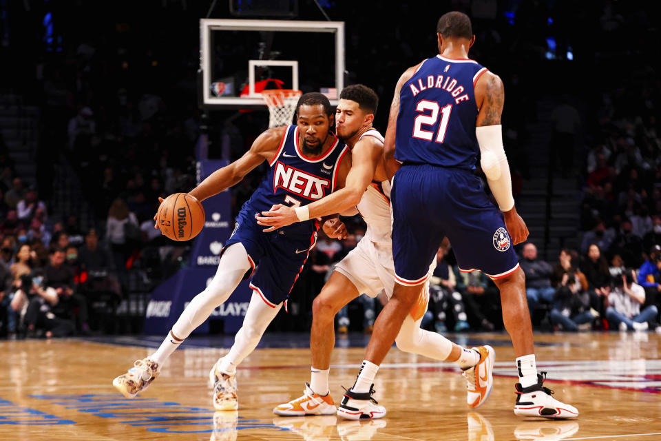 Brooklyn Nets forward Kevin Durant (7) drives against Phoenix Suns guard Devin Booker, center, as Nets forward LaMarcus Aldridge (21) looks on during the first half of an NBA basketball game, Saturday, Nov. 27, 2021, in New York. (AP Photo/Jessie Alcheh)