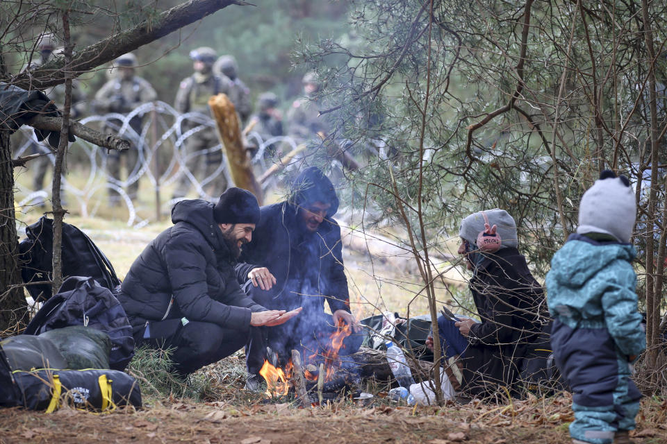 Migrants from the Middle East and elsewhere warm up by the fire as they gather at the Belarus-Poland border near Grodno, Belarus, Monday, Nov. 8, 2021. Poland increased security at its border with Belarus, on the European Union's eastern border, after a large group of migrants in Belarus appeared to be congregating at a crossing point, officials said Monday. The development appeared to signal an escalation of a crisis that has being going on for months in which the autocratic regime of Belarus has encouraged migrants from the Middle East and elsewhere to illegally enter the European Union, at first through Lithuania and Latvia and now primarily through Poland. (Leonid Shcheglov/BelTA via AP)