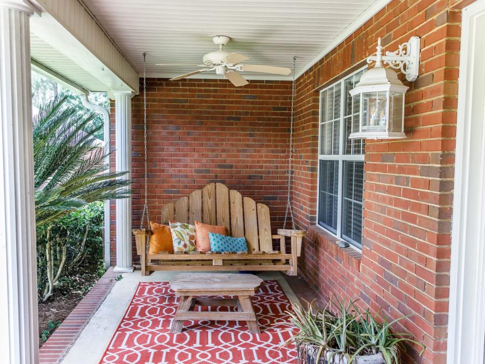 A wooden porch swing hanging on the porch of a brick house