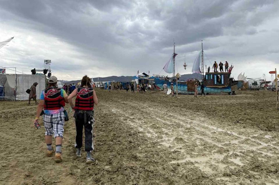 <p>JULIE JAMMOT/AFP via Getty</p>  Attendees walk through a muddy desert plain on September 2, 2023, after heavy rains turned the annual Burning Man festival site in Nevada