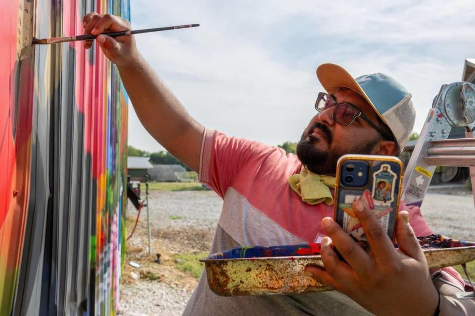 Isaac Tapia follows a design he keeps on his mobile phone while finishing a mural called “What’s The Sword”. The mural was made for The BoysGrow Program in Kansas City. Emily Curiel/Emily Curiel