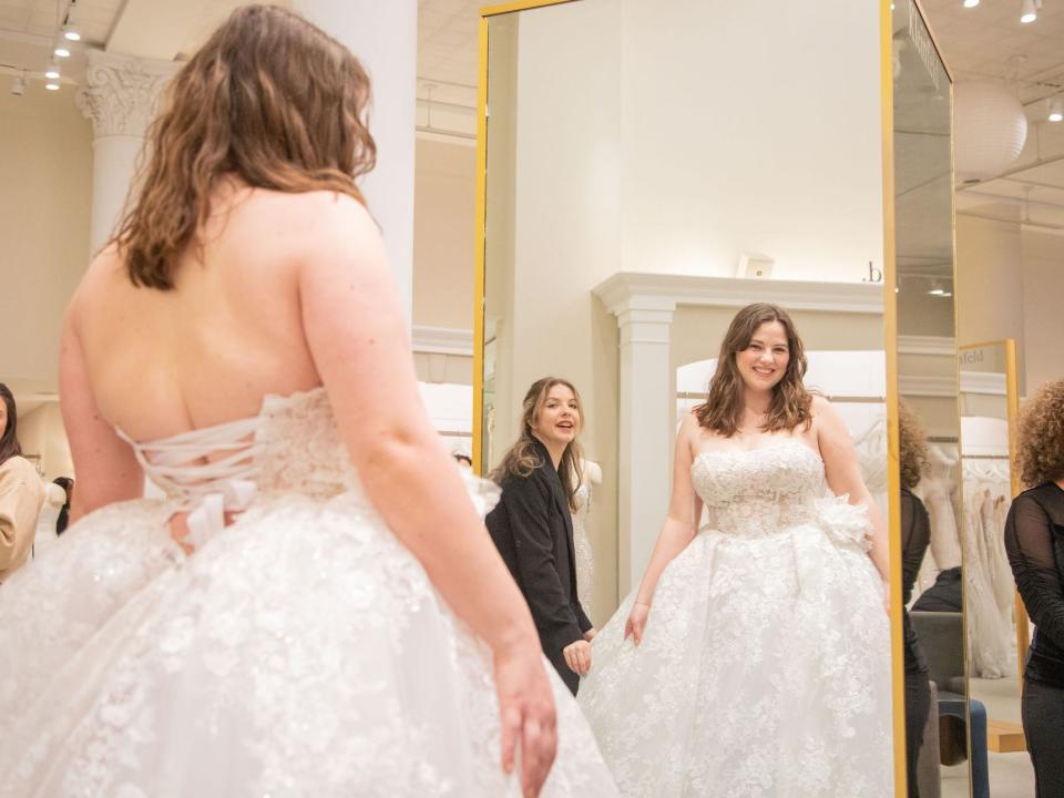 A woman looks at herself in a mirror as she wears a ball gown wedding dress.