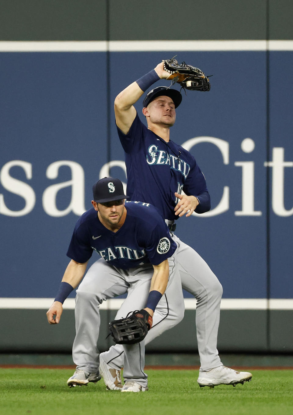 Seattle Mariners center fielder Jarred Kelenic, top, catches a fly ball from Kansas City Royals' Andrew Benintendi as right fielder Mitch Haniger, bottom, avoids the play during the third inning of a baseball game at Kauffman Stadium in Kansas City, Mo., Saturday, Sept. 18, 2021. (AP Photo/Colin E. Braley)