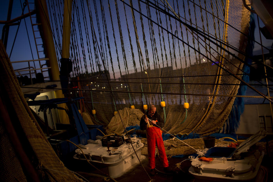 FILE- In this Friday, March 3, 2017 file photo, a fisherman works on his ship fixing a fishing net at the port in The Hague, The Netherlands. Fishing has become one of the main stumbling blocs in the Brexit negotiations for a new trade deal between the European Union and the United Kingdom. (AP Photo/Emilio Morenatti, File)