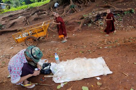 Buddhist novice monks walk past a drug user in Man Sam, northern Shan state, Myanmar July 11 , 2016. REUTERS/Soe Zeya Tun