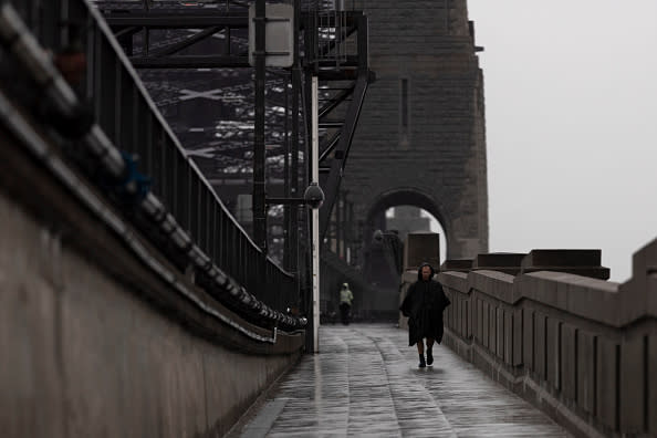 A man walks across the Sydney Harbour Bridge under heavy rain.