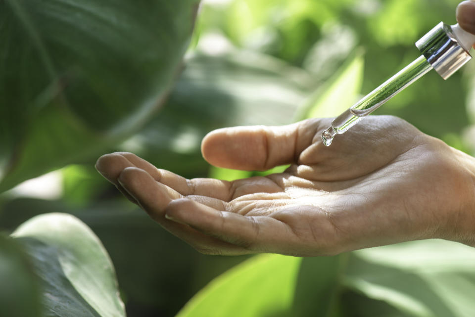 Hand by plants and nature with oil dropper hovering above hand.